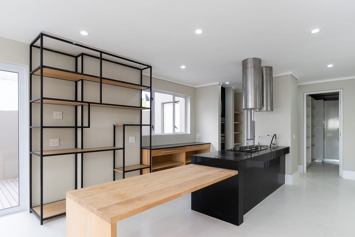 Modern kitchen featuring a black island with integrated gas hob, stainless steel extractor fan, and custom built-in shelving units.