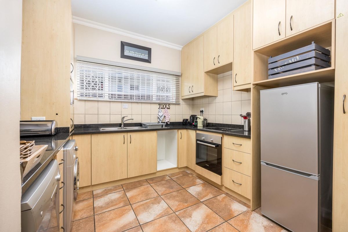 Functional kitchen featuring light wood cabinetry, dark granite countertops, tiled backsplash, built-in oven, and integrated space for laundry appliances.