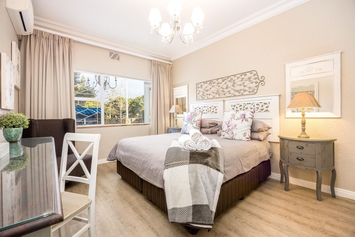 A well-maintained bedroom featuring wood-look flooring, crown molding, a wall-mounted air conditioning unit, and a large window providing natural light.