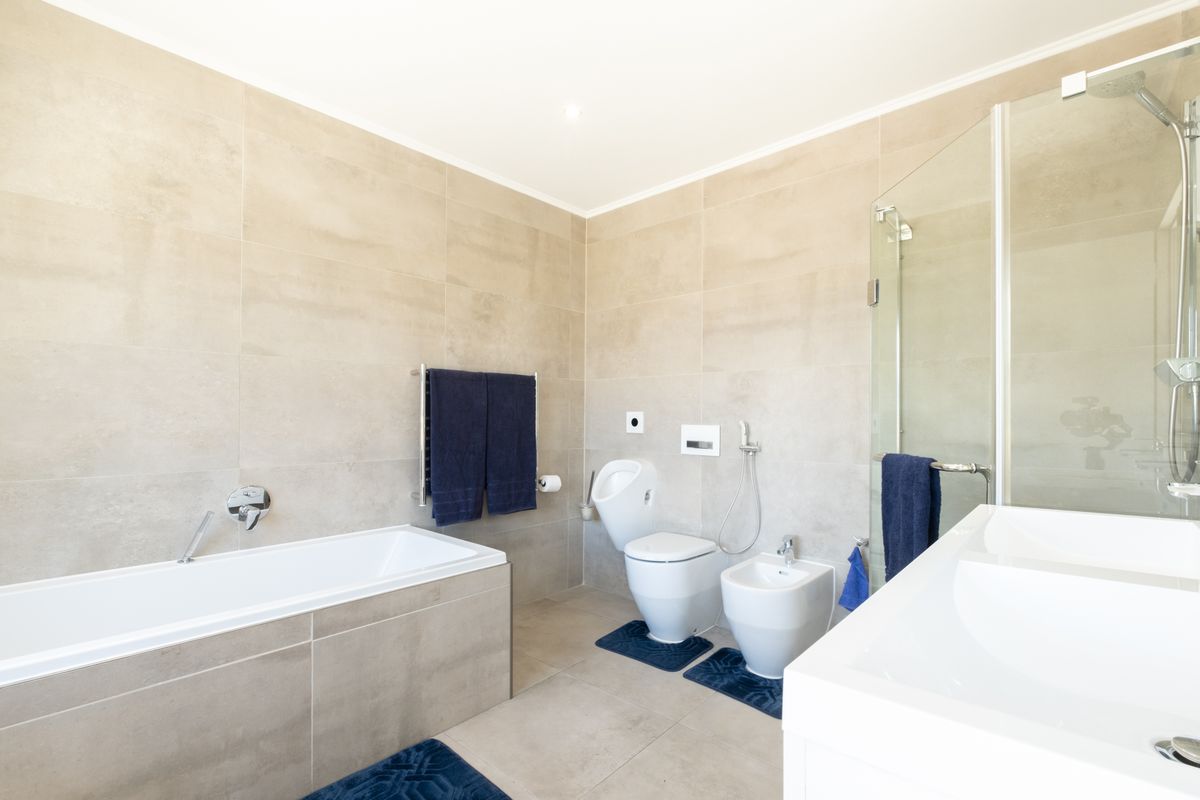 Modern bathroom featuring a built-in bathtub, glass-enclosed shower, wall-mounted toilet, bidet, and neutral large-format floor and wall tiling.