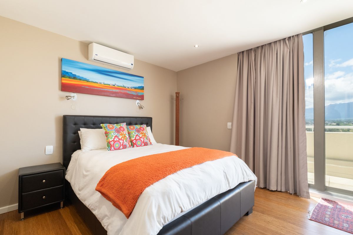 A well-maintained bedroom featuring timber flooring, a wall-mounted air conditioning unit, and floor-to-ceiling glass sliding doors leading to a private balcony.