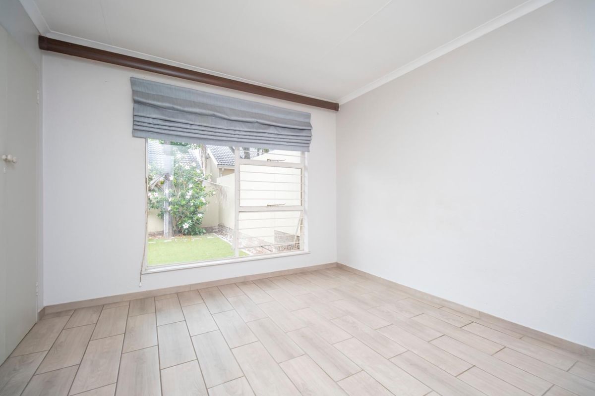 A bright, empty bedroom featuring light wood-look tile flooring, neutral walls, and a large window overlooking the rear garden.