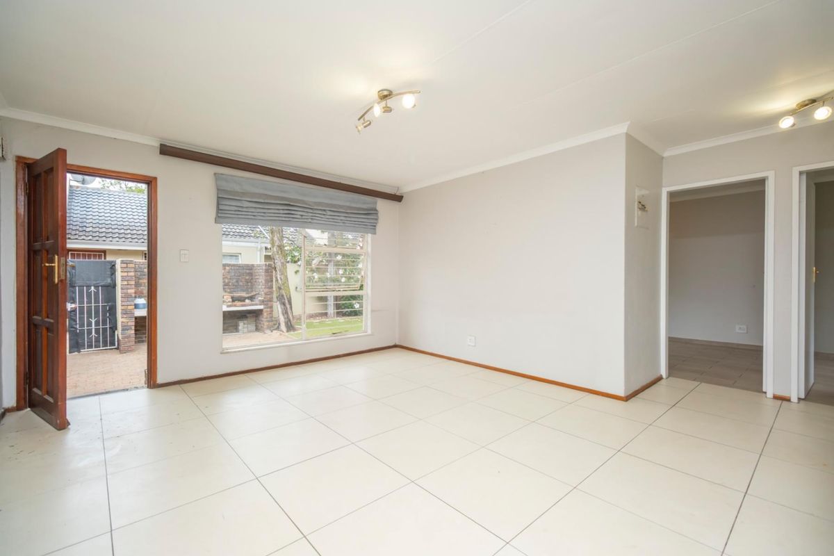 A bright, open-plan living area featuring neutral tiled flooring, large windows, and direct access to an outdoor patio space.