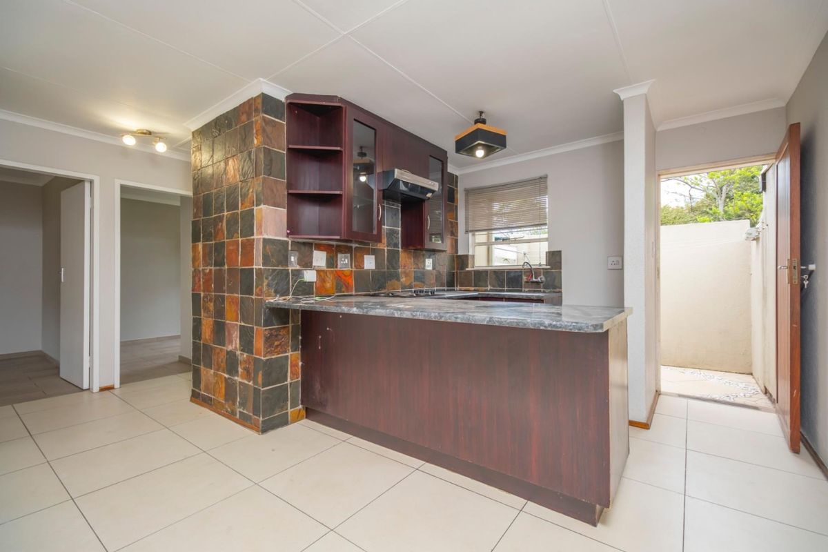 A functional kitchen featuring dark wood cabinetry, a stone-tiled feature wall, a breakfast bar, and tiled flooring with direct access to an outdoor area.