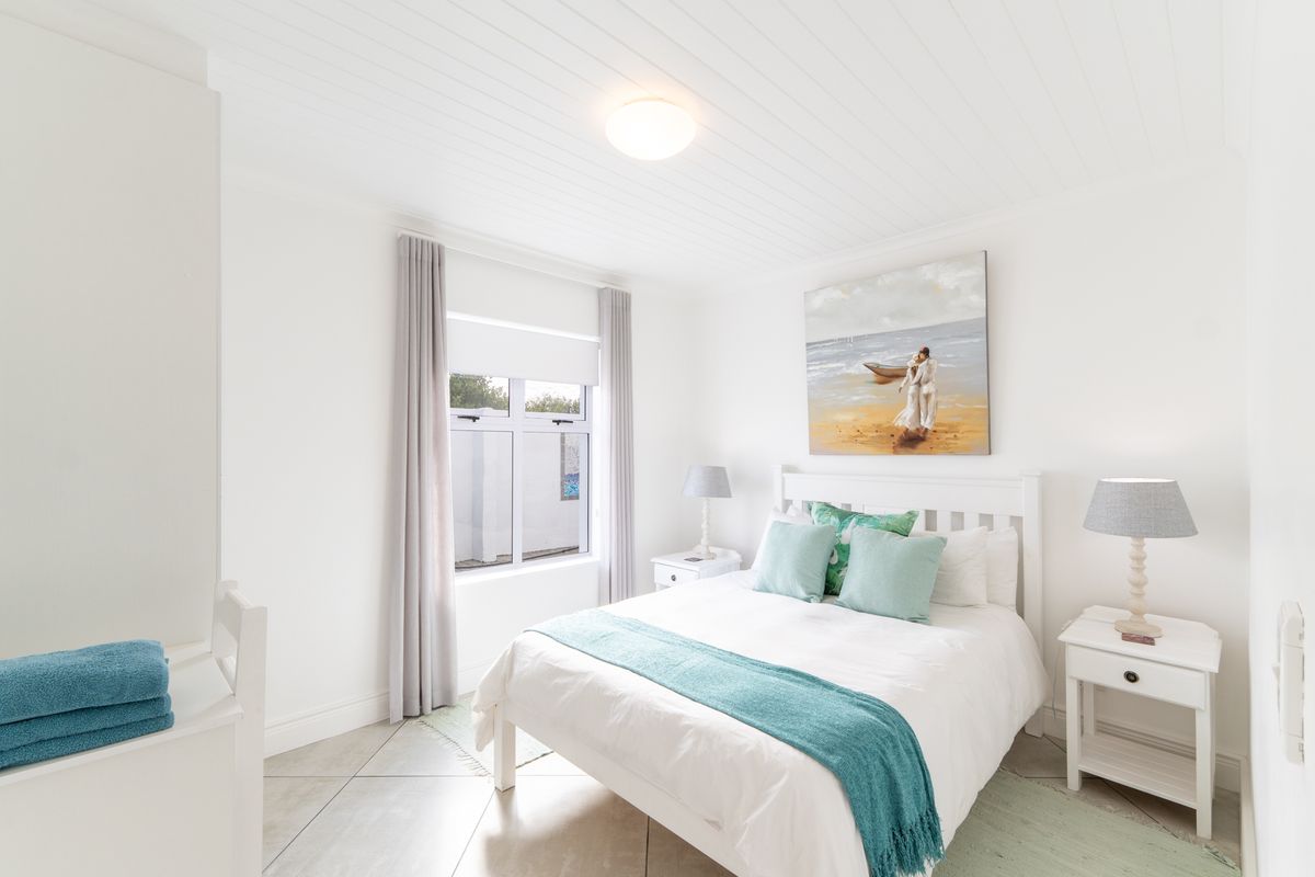 A bright and well-maintained bedroom featuring tiled flooring, a tongue-and-groove ceiling, and a window with neutral curtains.