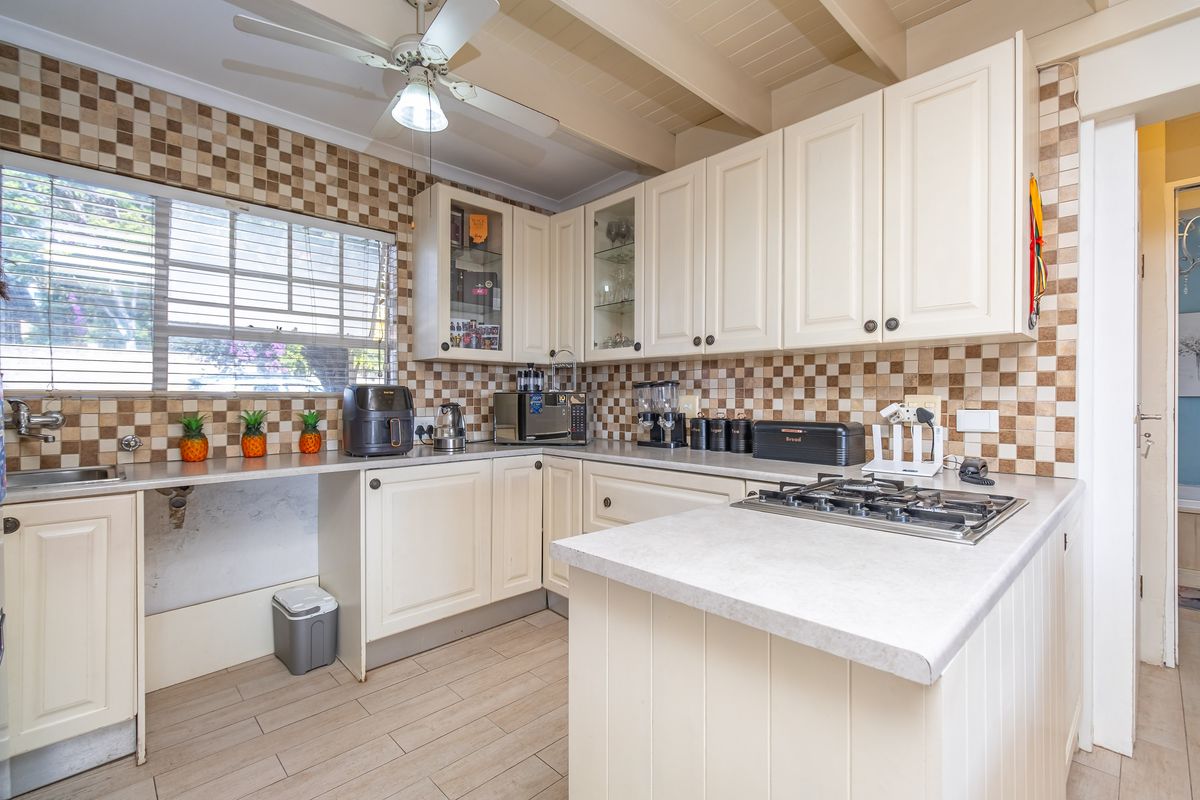 A functional kitchen featuring cream cabinetry, a gas hob, tiled backsplash, and a ceiling fan, offering a classic layout with ample counter space.