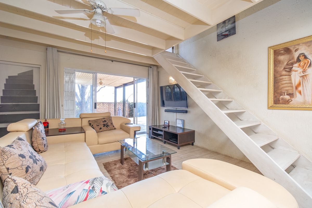 A living room featuring exposed timber ceiling beams, a staircase, and sliding glass doors leading to an outdoor patio area.
