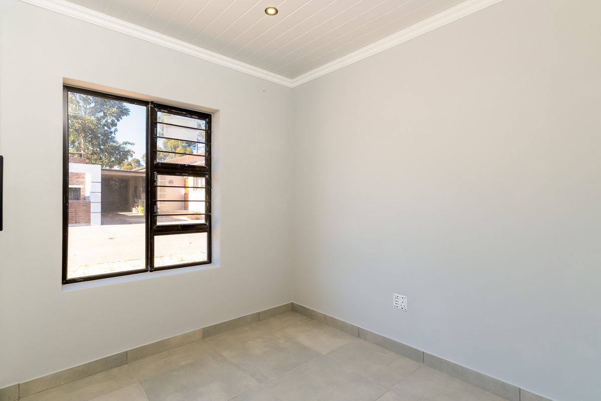 A bright, empty bedroom featuring neutral tiled flooring, a modern tongue-and-groove ceiling, and a large window with security bars.