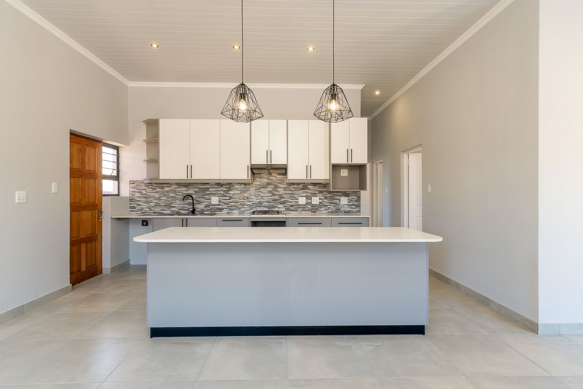Modern open-plan kitchen featuring a central island, stone countertops, mosaic tile backsplash, and sleek cabinetry with integrated lighting.