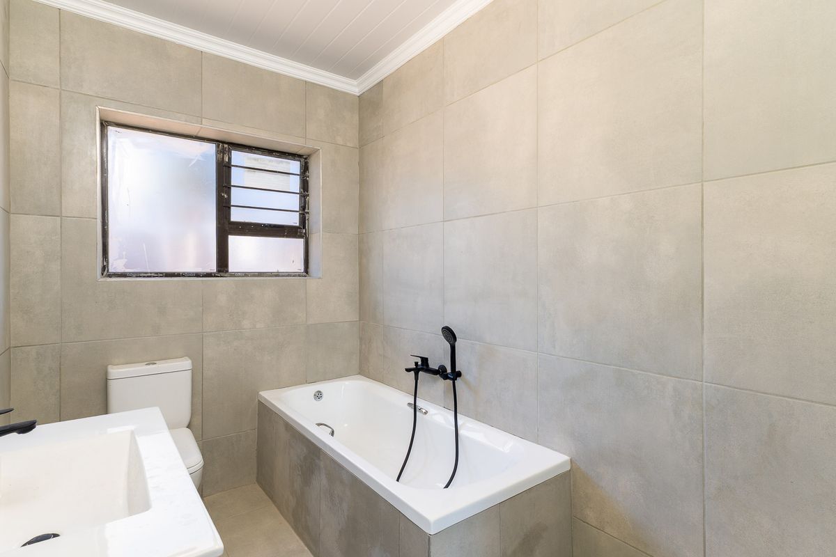 Modern bathroom featuring large format neutral wall tiles, a built-in bathtub with matte black fixtures, and a contemporary vanity basin.