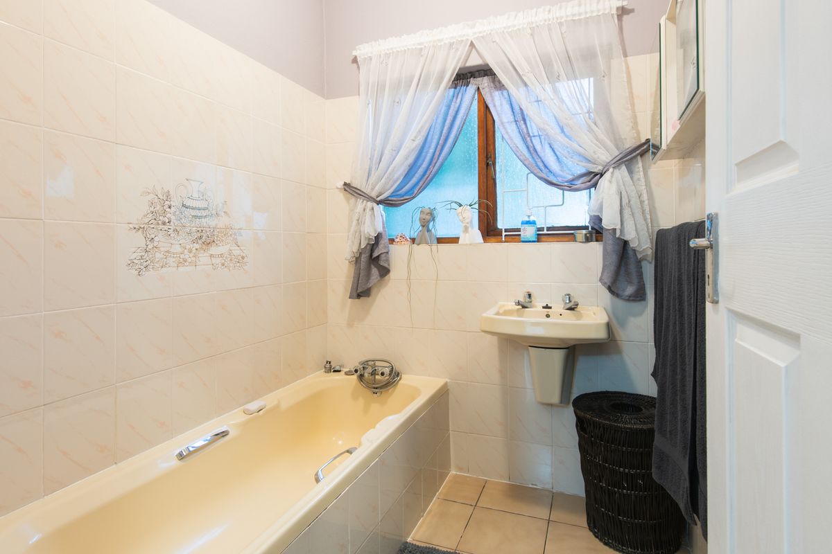 A dated bathroom featuring a built-in bathtub, wall-mounted basin, and tiled walls, offering potential for a modern renovation.