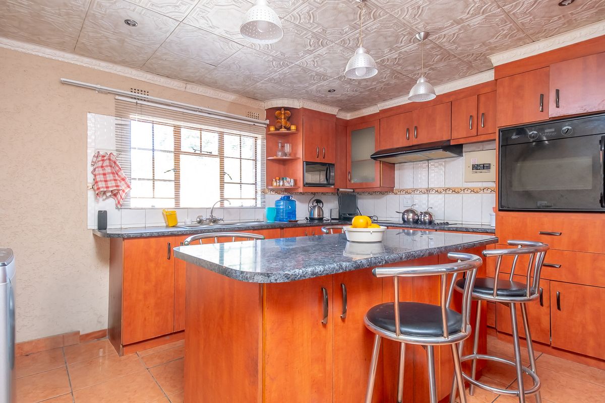A functional kitchen featuring wood-finish cabinetry, a central island with stone-look countertop, built-in oven, and tiled splashback.