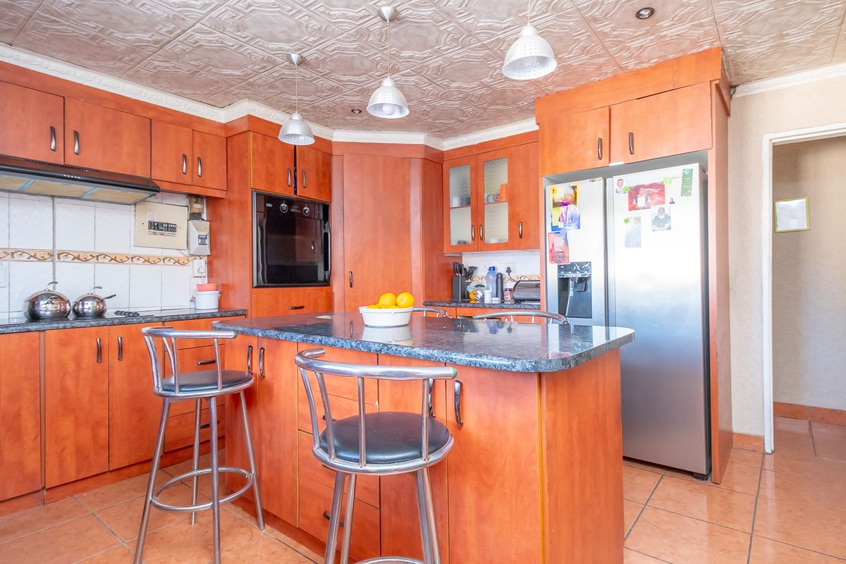 A functional kitchen featuring wood-toned cabinetry, a central island with stone countertops, built-in oven, and tiled flooring.