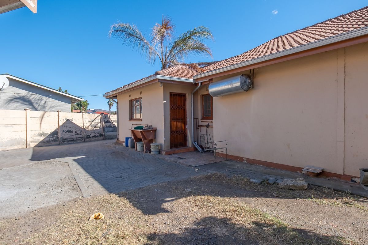 Rear exterior view of the property featuring a paved courtyard, external geyser, and security gate access.