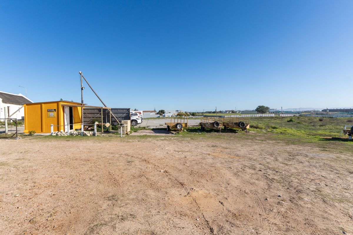 Expansive outdoor business yard featuring a small yellow office structure, gravel parking area, and open land suitable for storage or commercial operations.