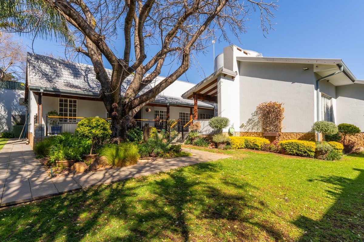 A view of the rear exterior of the house featuring a landscaped garden, paved walkway, and covered patio area.