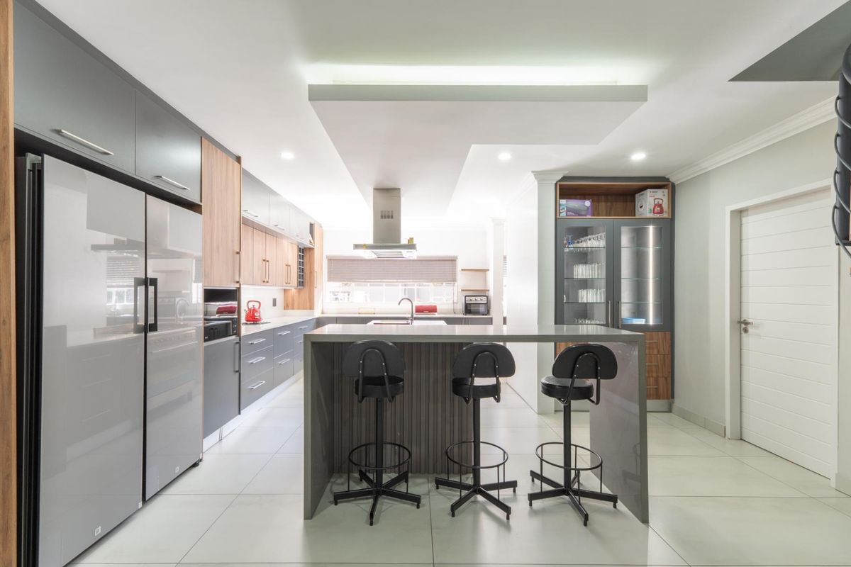 Modern kitchen featuring a central island with breakfast bar, sleek cabinetry, integrated appliances, and a contemporary bulkhead ceiling with recessed lighting.