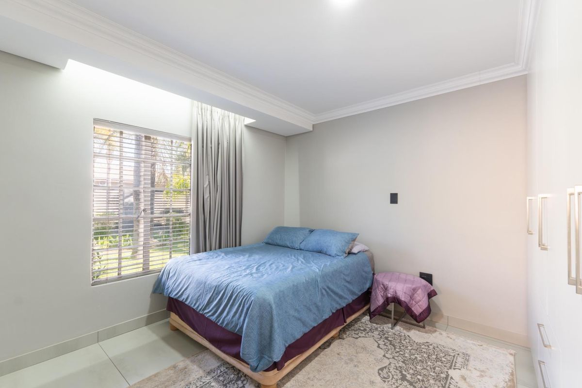 A bright bedroom featuring tiled flooring, built-in cabinetry, and a large window with integrated blinds, offering a clean and functional living space.