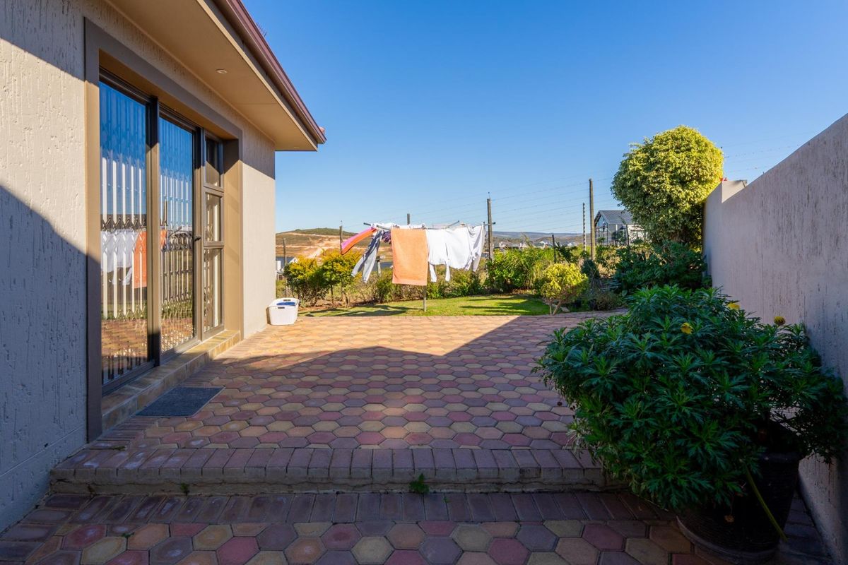 A paved rear patio area featuring sliding glass doors, established garden borders, and perimeter fencing.