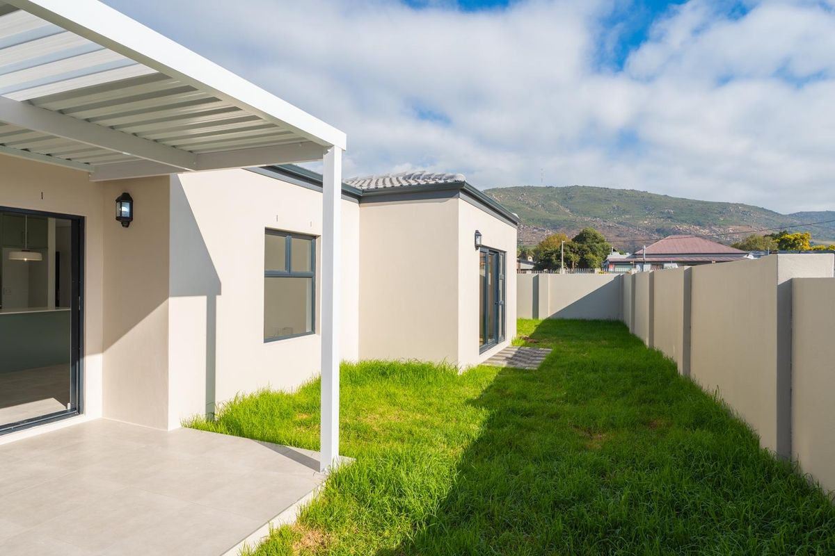A modern rear exterior view featuring a covered patio with tiled flooring, a well-maintained lawn, and perimeter boundary walls.