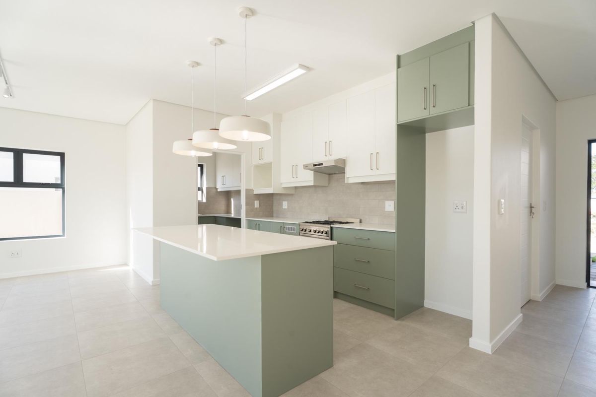 Modern open-plan kitchen featuring sage green and white cabinetry, a central island with stone countertops, and integrated stainless steel appliances.