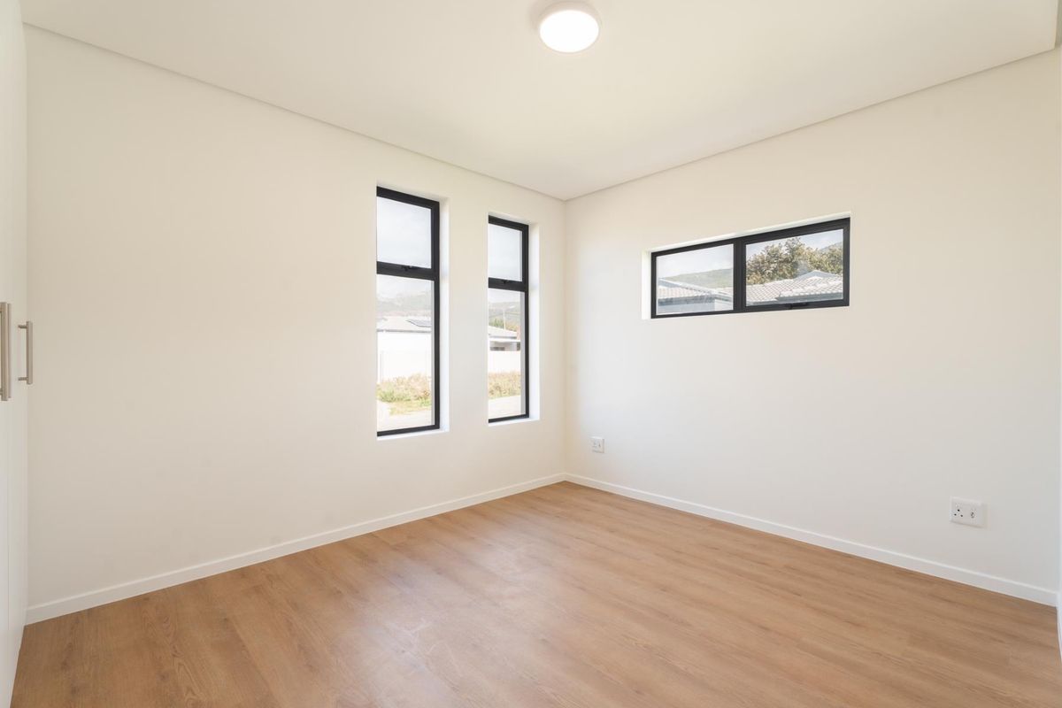A bright, empty bedroom featuring modern wood-look flooring, neutral walls, and black-framed windows providing natural light.