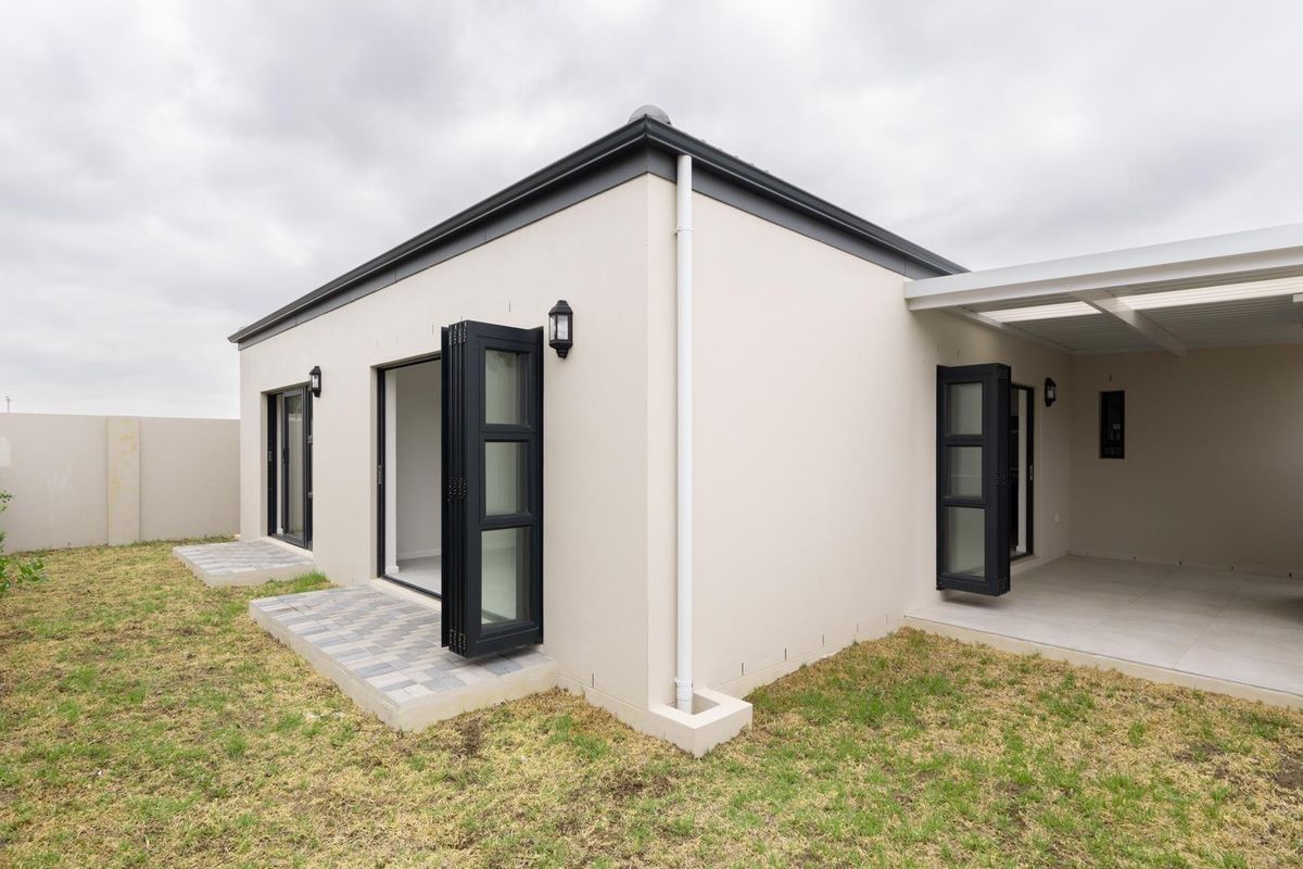 Rear view of the property featuring a covered patio, paved walkways, and modern black-framed folding doors leading into the interior.
