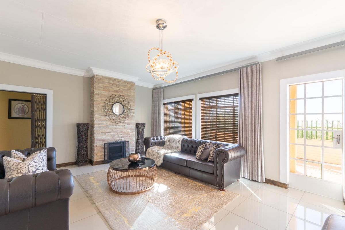 A well-maintained living room featuring a stone-clad fireplace, tiled flooring, and large windows with wooden blinds, offering a bright and inviting atmosphere.