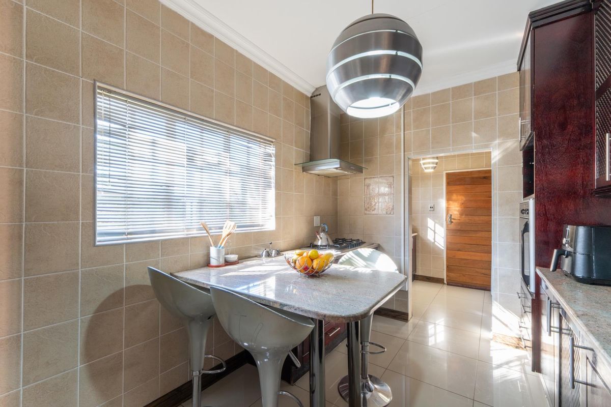 A functional kitchen featuring tiled walls, granite countertops, a built-in gas hob, extractor fan, and an integrated oven, with an adjacent scullery area.