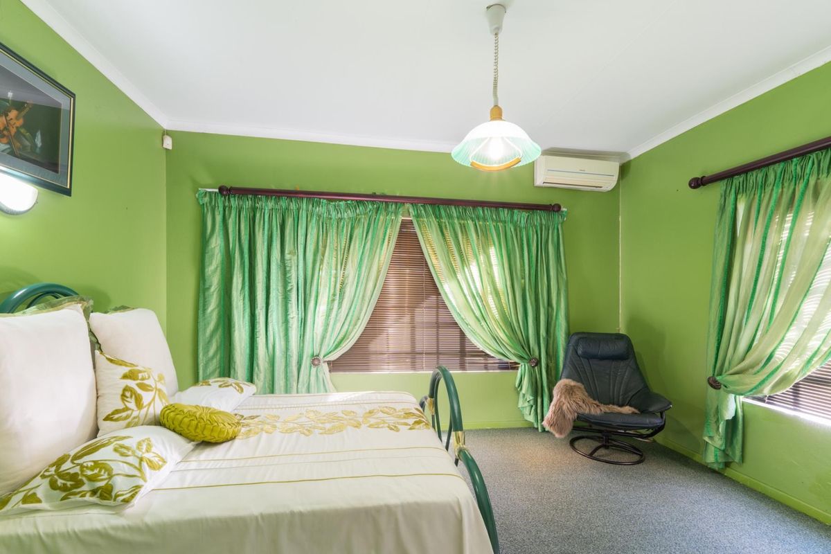 A bedroom featuring green painted walls, carpeted flooring, a wall-mounted air conditioning unit, and window treatments.
