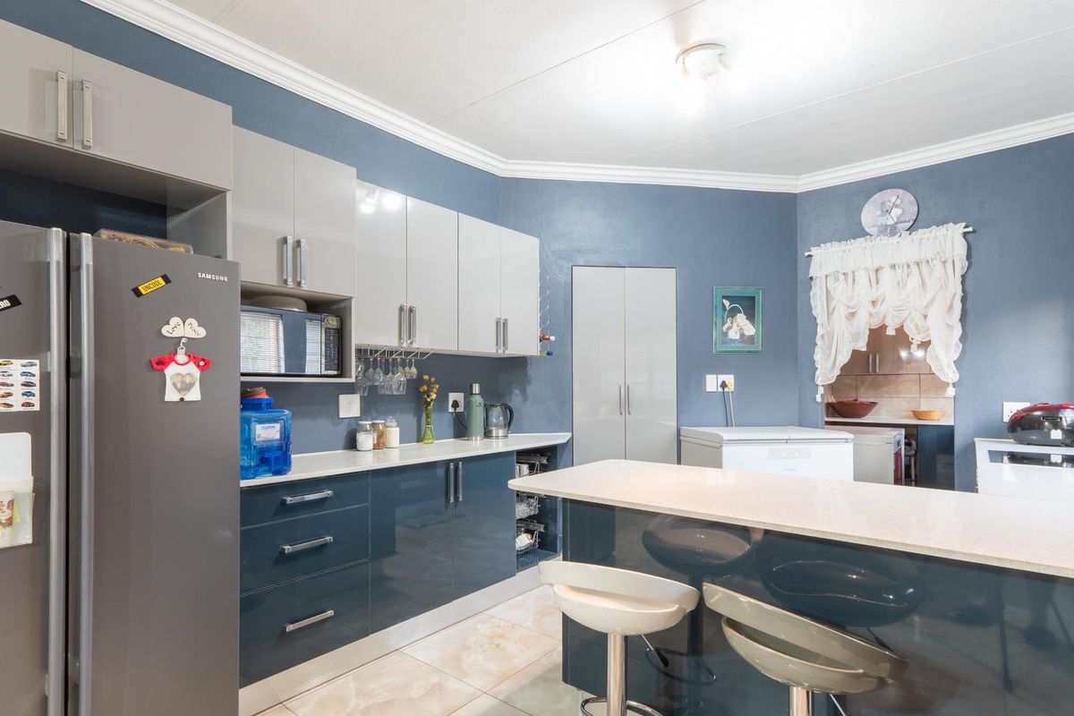 Modern kitchen featuring high-gloss cabinetry, stone countertops, a central island with breakfast bar seating, and tiled flooring.