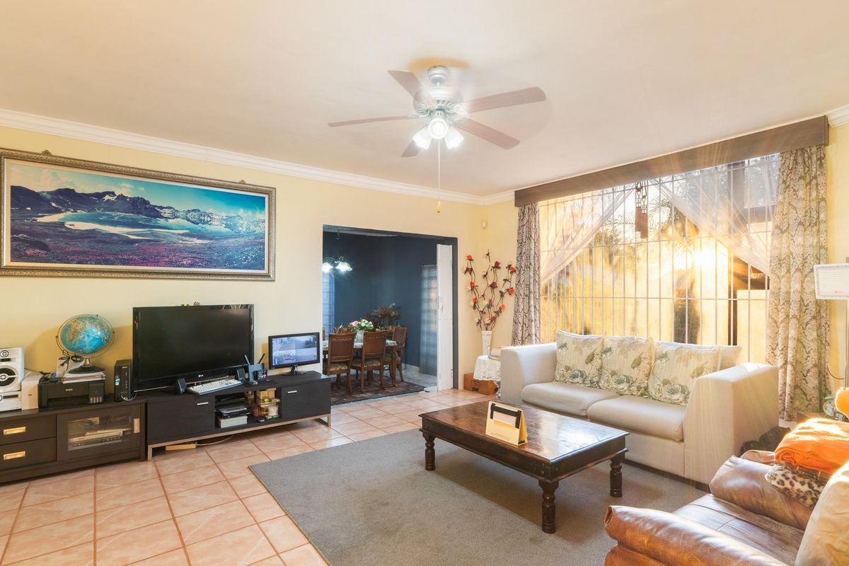 Spacious living room featuring tiled flooring, a ceiling fan, and large windows with security bars, offering a view into the adjacent dining area.