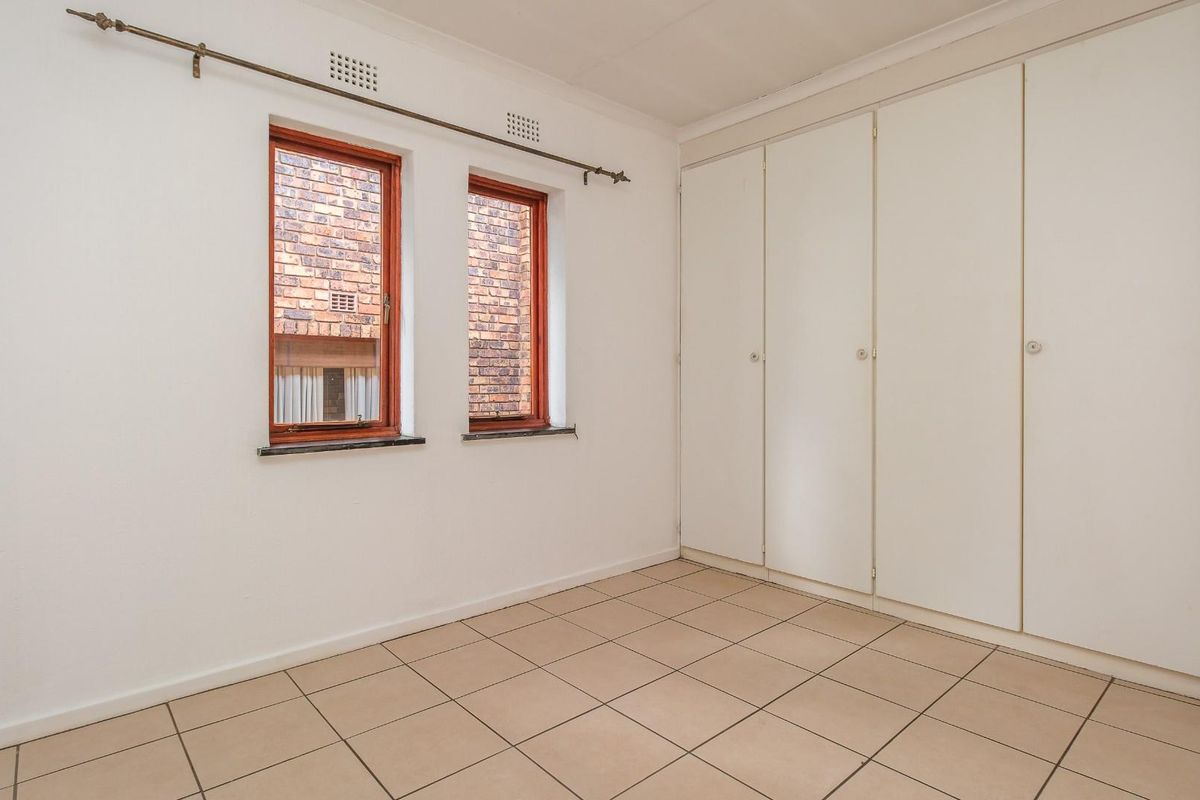 An empty bedroom featuring tiled flooring, built-in cupboards, and two windows with wooden frames.