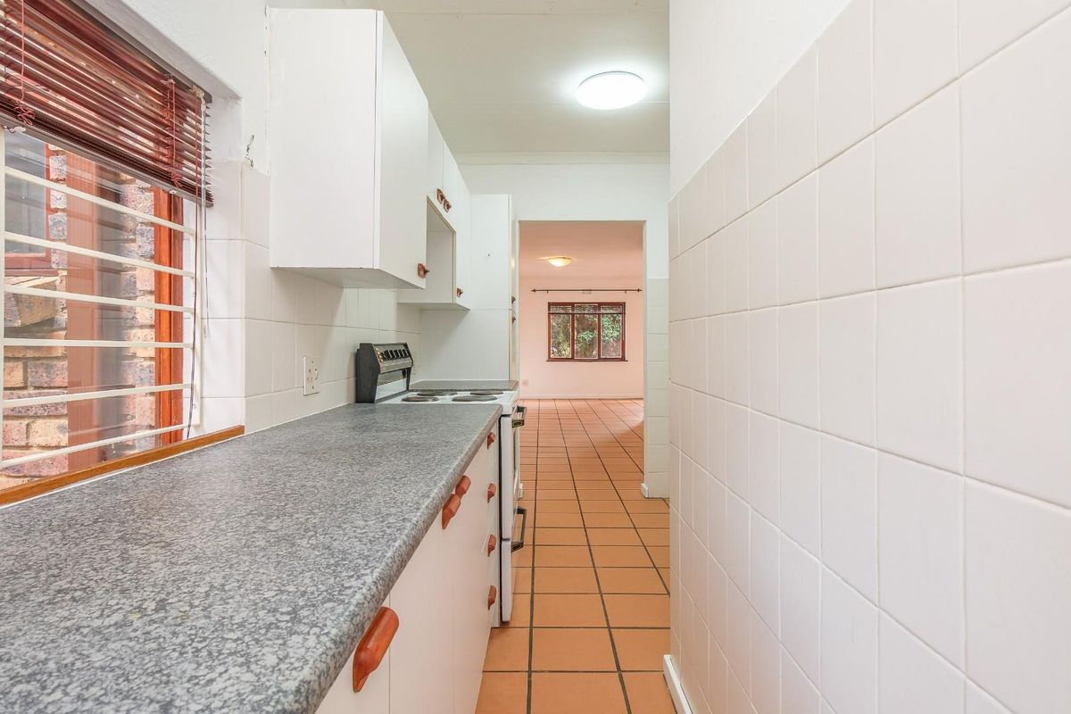 A functional galley-style kitchen featuring white cabinetry, granite-look countertops, and tiled flooring, leading through to an open-plan living area.