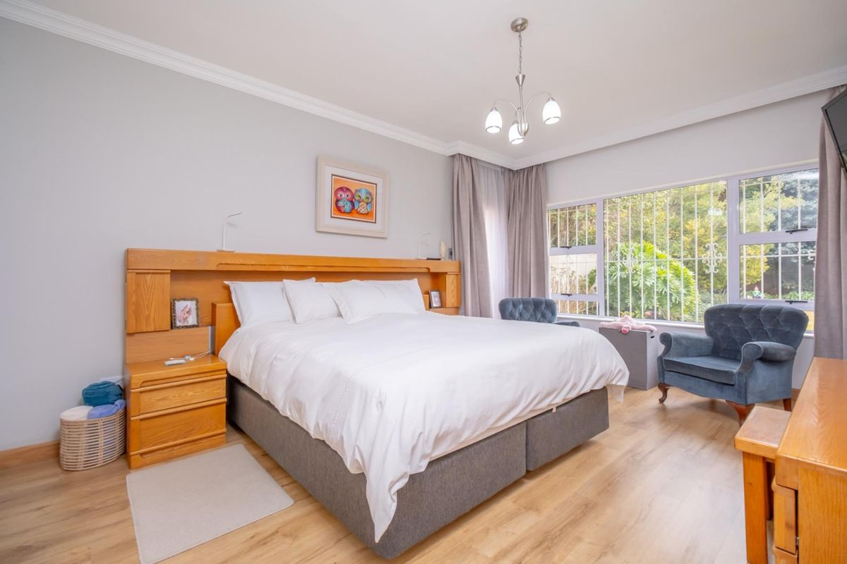 A well-maintained bedroom featuring a built-in wooden headboard with integrated bedside tables, laminate flooring, and large windows with security bars.