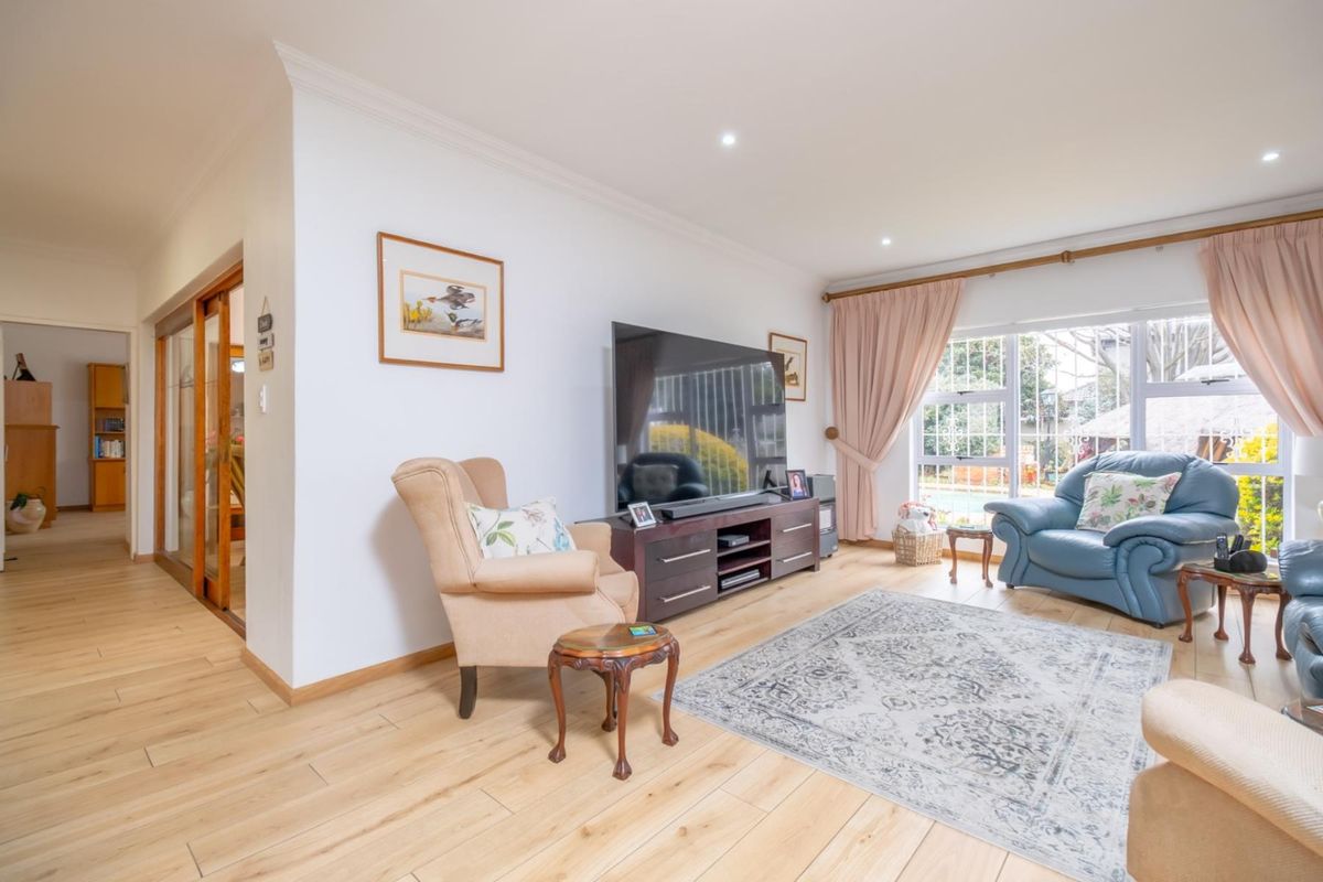 A bright living room featuring light wood-look flooring, recessed downlighting, and large windows providing natural light and garden views.