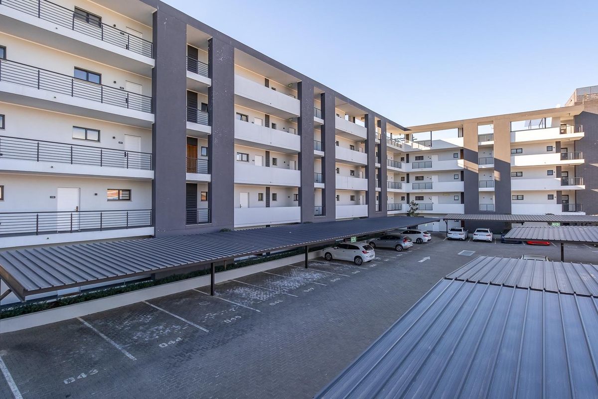 Exterior view of a modern multi-story apartment complex featuring covered parking bays and private balconies for each unit.