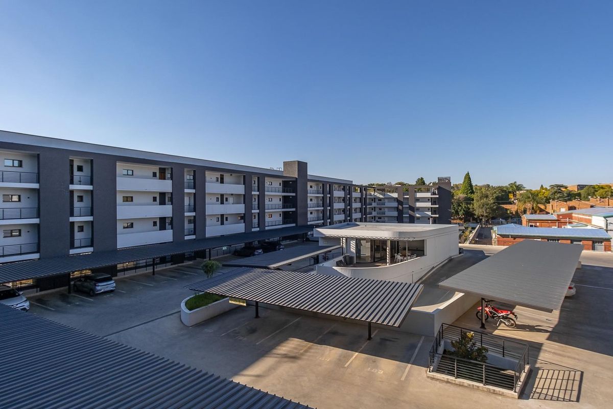 Aerial view of the apartment complex featuring multi-level residential blocks, paved parking areas with covered carports, and a central clubhouse facility.
