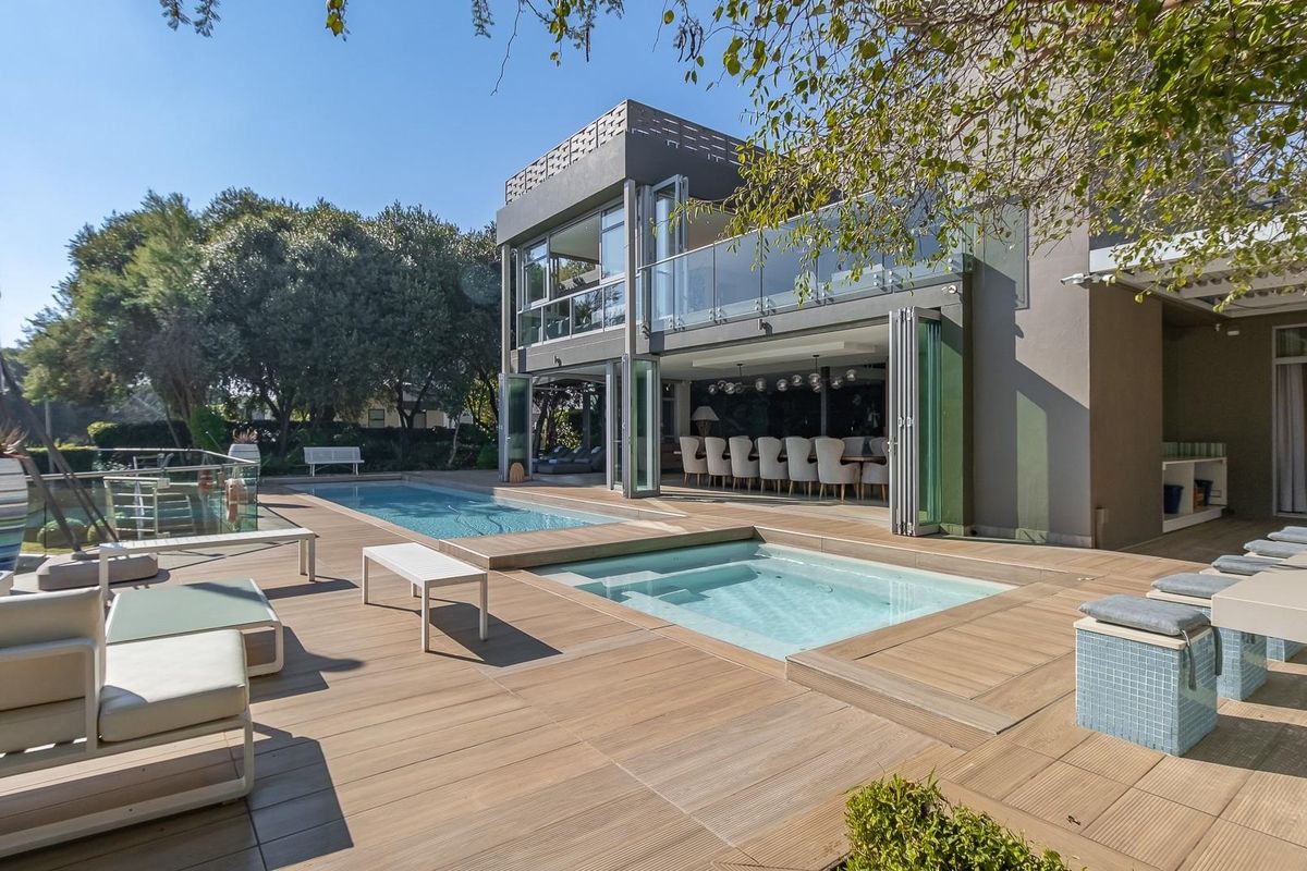 Modern rear exterior featuring a swimming pool, integrated spa, and expansive timber decking with seamless indoor-outdoor flow through large folding glass doors.
