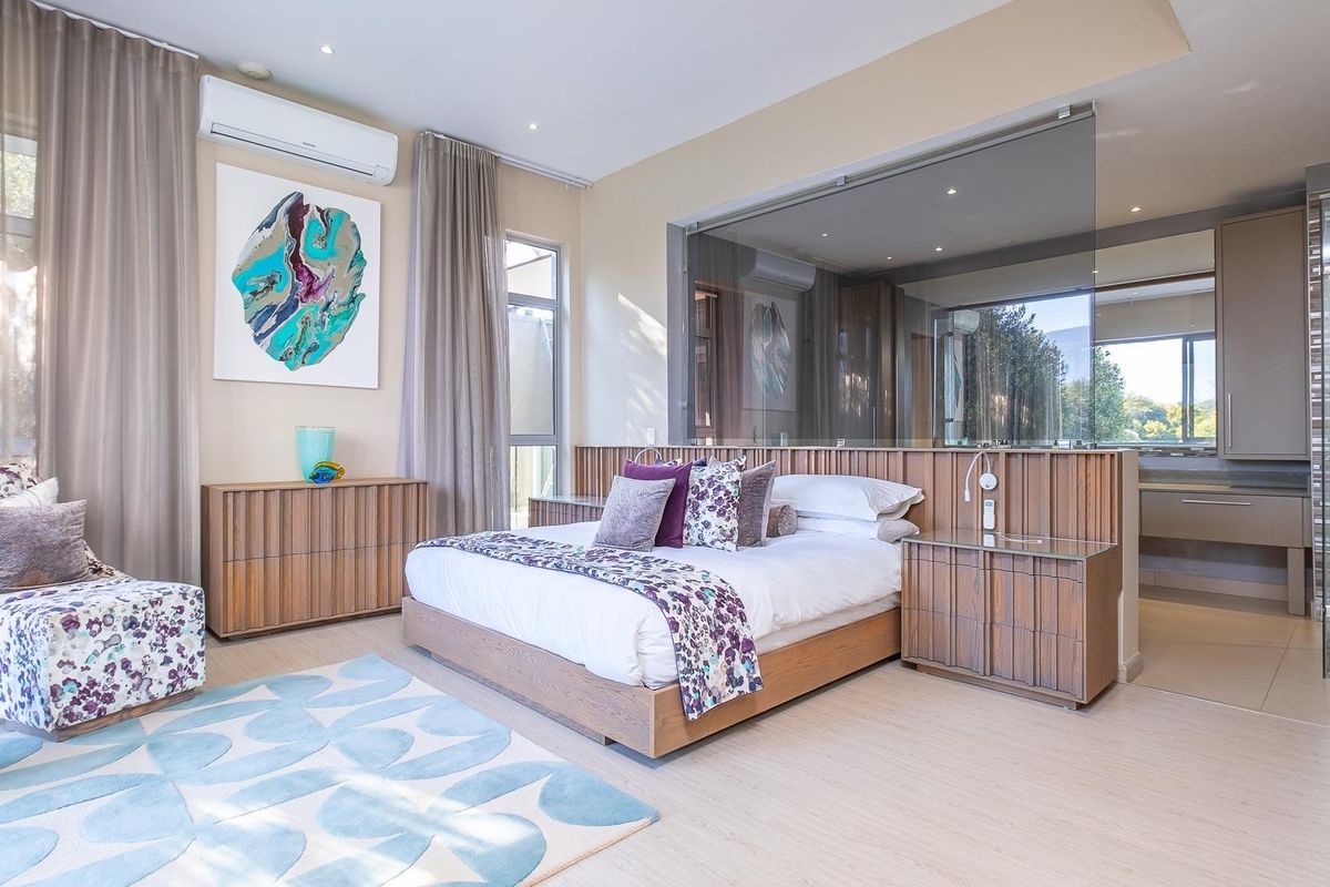Spacious master bedroom featuring a glass-partitioned en-suite bathroom, built-in timber cabinetry, recessed lighting, and a wall-mounted air conditioning unit.
