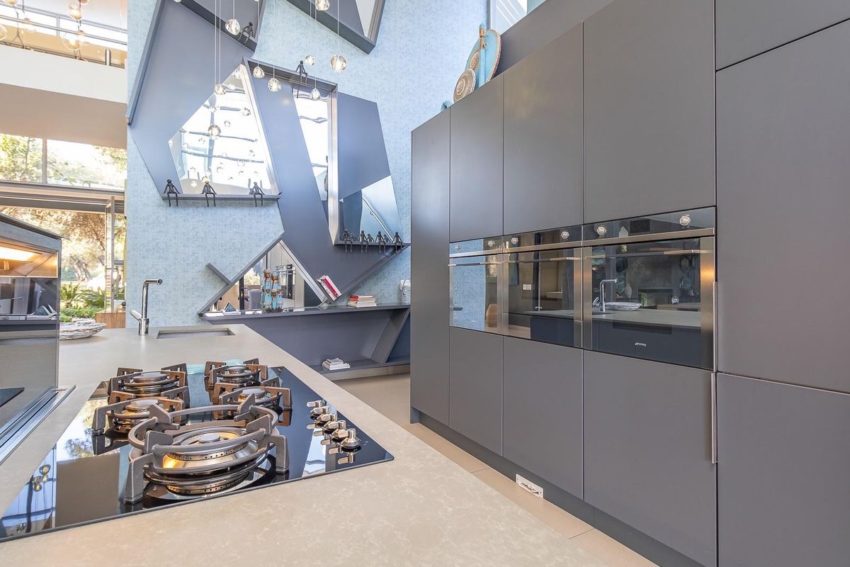 Modern kitchen featuring high-end integrated appliances, sleek dark cabinetry, and a spacious island with a built-in gas hob, set against a unique architectural feature wall.
