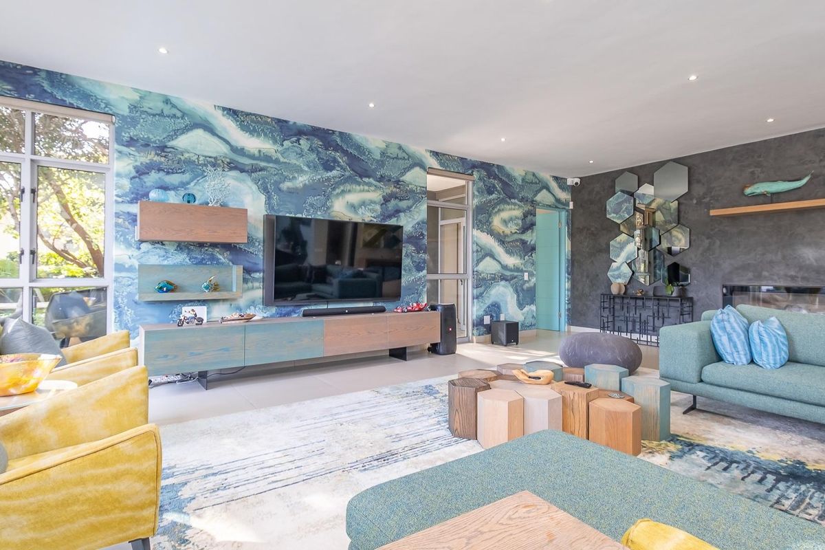 Spacious living room featuring a striking blue patterned feature wall, recessed ceiling lighting, and a modern fireplace with a decorative mirror installation.