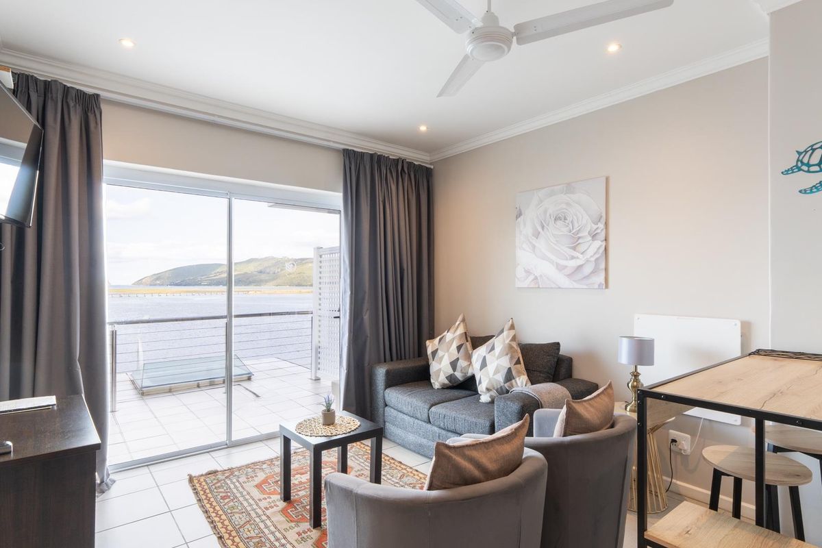 A bright living room featuring tiled floors, a ceiling fan, and large sliding glass doors that open onto a balcony with scenic water views.
