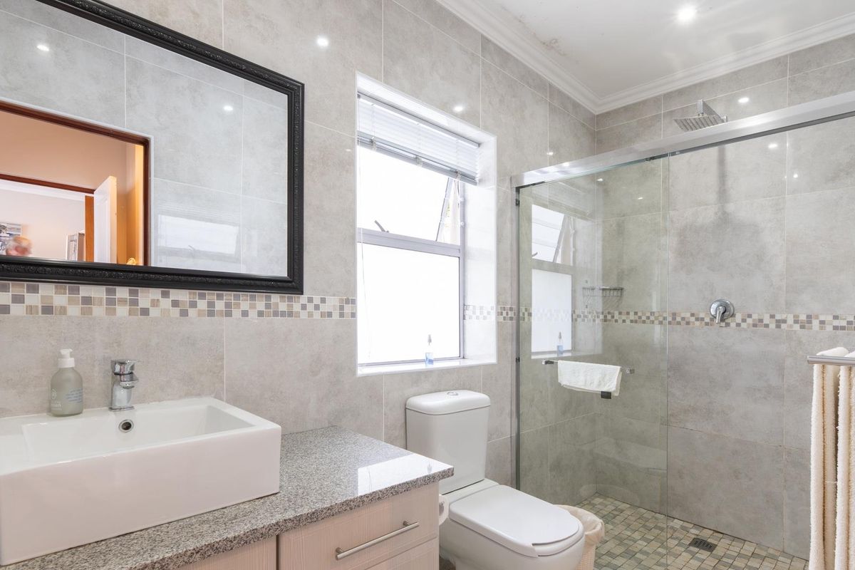 Modern bathroom featuring a vessel sink on a granite vanity, a glass-enclosed shower with a rain shower head, and neutral ceramic wall tiling.
