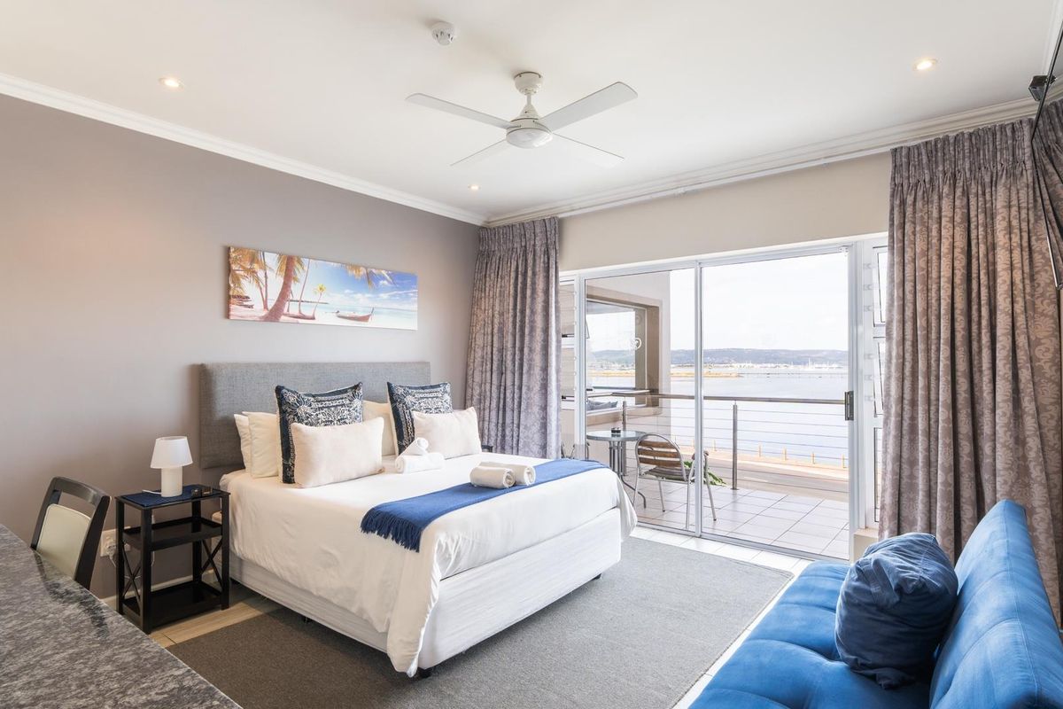 A well-maintained bedroom featuring a ceiling fan, recessed lighting, and a sliding glass door that opens onto a balcony with water views.