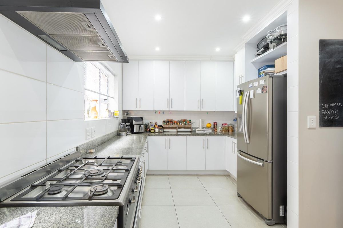 A modern, well-maintained kitchen featuring white cabinetry, granite countertops, a gas hob with an extractor fan, and tiled flooring.