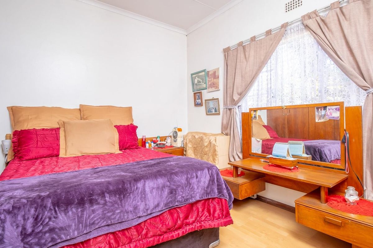A bedroom featuring light-toned laminate flooring, a large window with curtains, and a built-in vanity unit.
