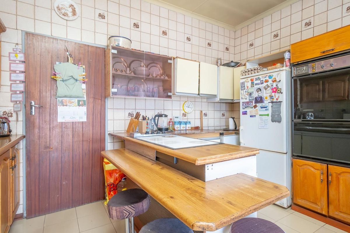 A dated kitchen featuring wooden cabinetry, integrated oven, and tiled walls with a breakfast bar counter.