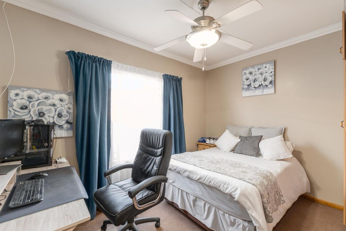 A functional bedroom featuring a ceiling fan, carpeted flooring, and a window with curtain treatments.