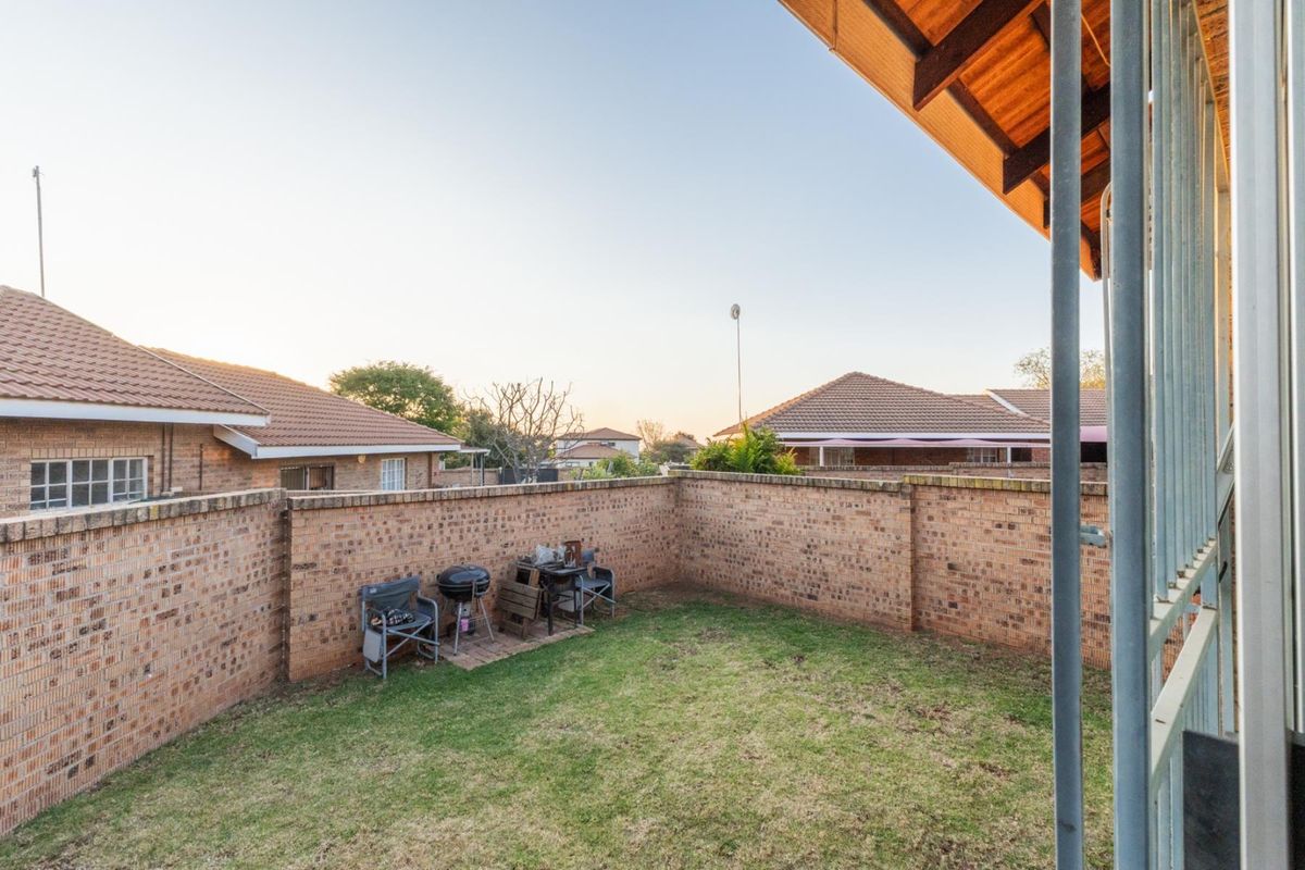 A private rear garden featuring a perimeter brick wall, a small grassed area, and a paved section, viewed from a covered patio.